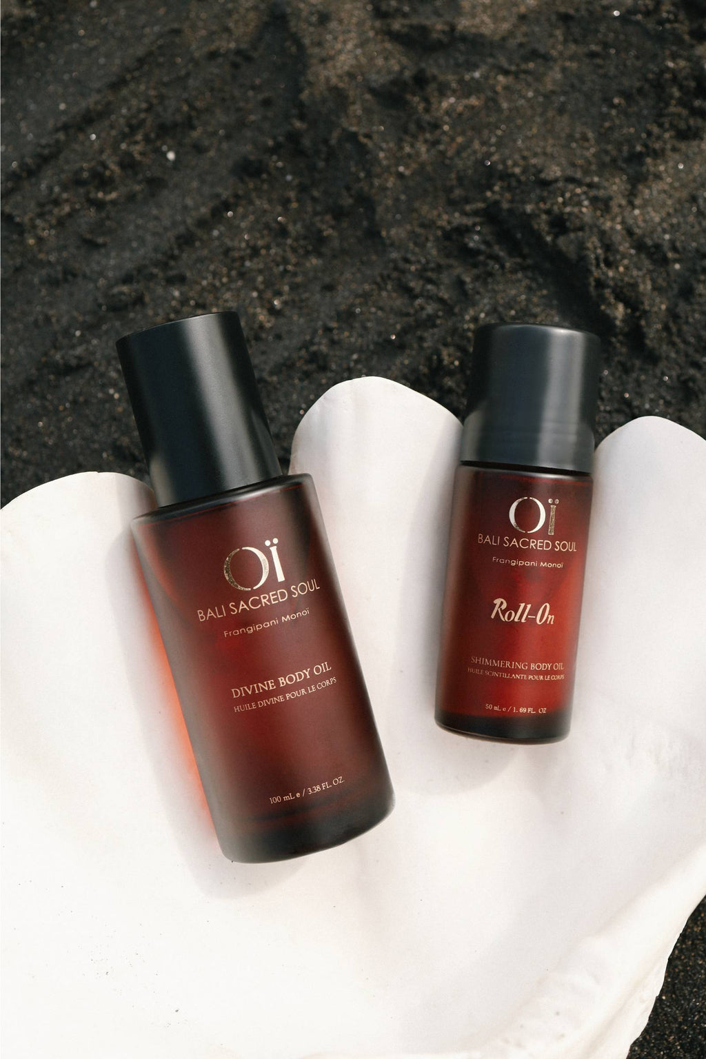 Flacons OÏ Divine et Roll-on dans un coquillage sur une plage de sable noir
